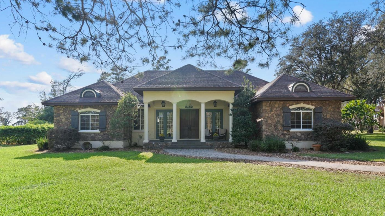 Front view of a luxury Winter Garden estate with a slate porch, grand wooden doors, and lush 5-acre wooded surroundings.