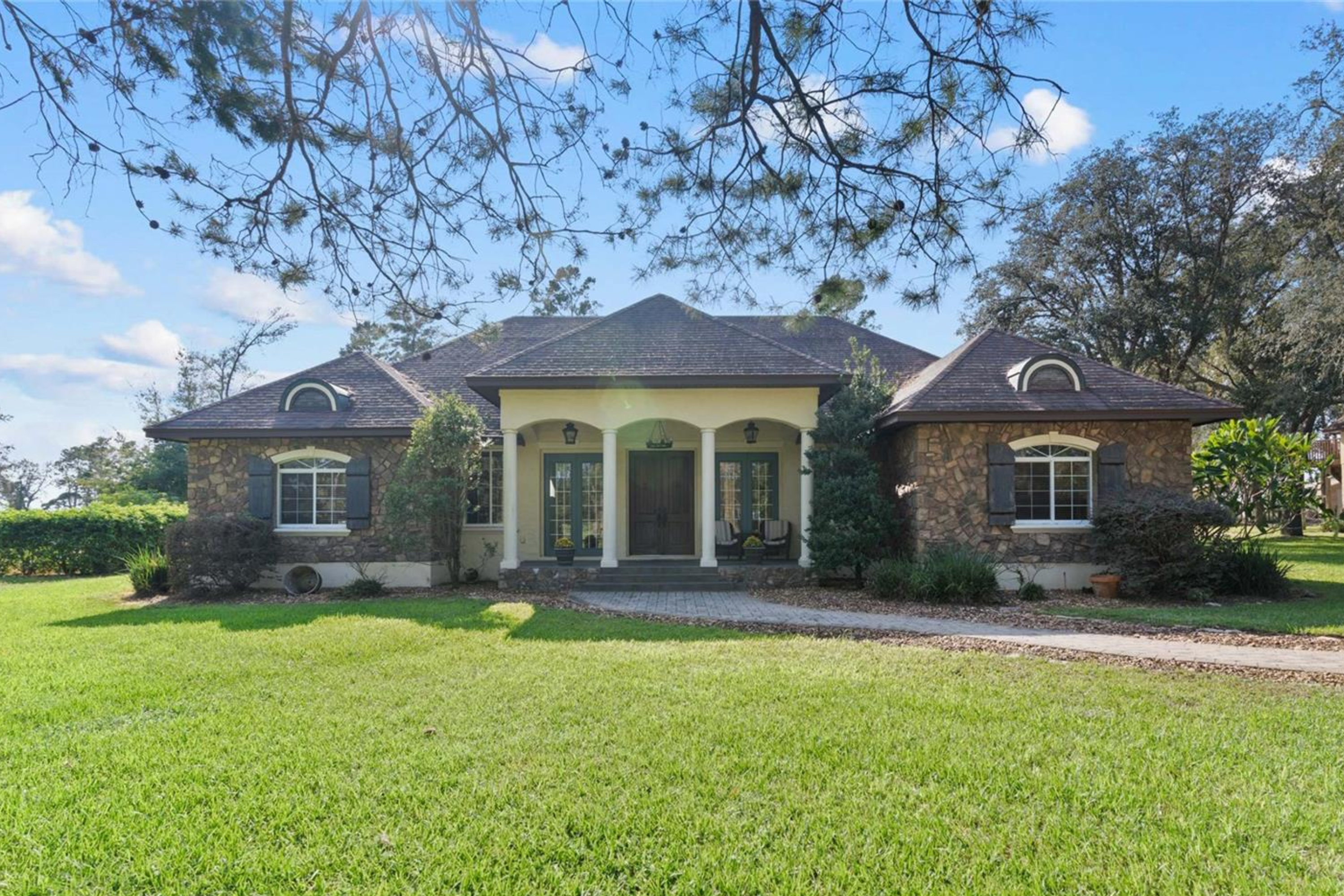 Front view of a luxury Winter Garden estate with a slate porch, grand wooden doors, and lush 5-acre wooded surroundings.