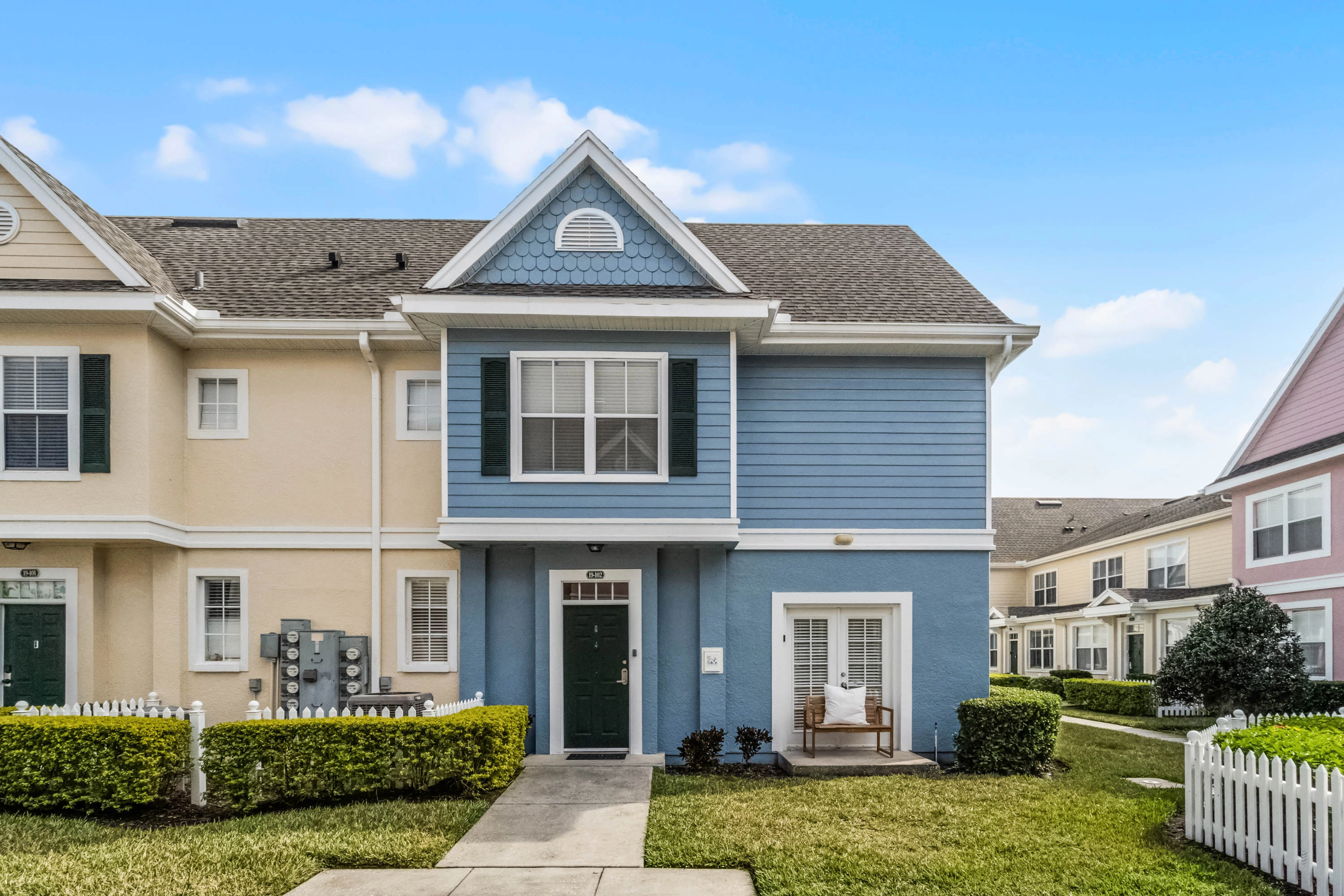 Charming two-story townhome in Kissimmee, FL, featuring a well-maintained exterior with a blue facade, white accents, and a welcoming front entry. Surrounded by manicured lawns, hedges, and neighboring townhomes, creating a cozy suburban feel.