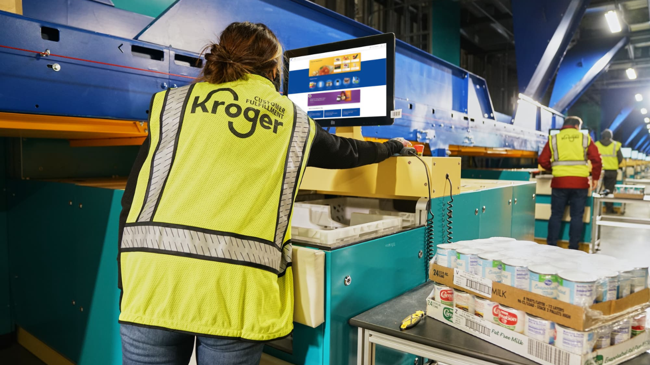 A Kroger employee managing AI-powered robots for fast and efficient grocery packing.
