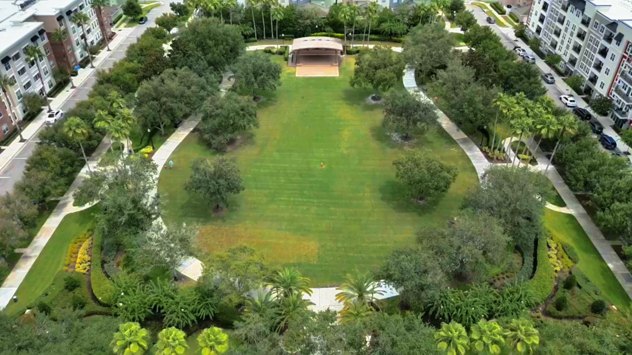 Aerial view of the park lawn and stage in Avalon Park, east Orlando, lined with trees and apartment buildings