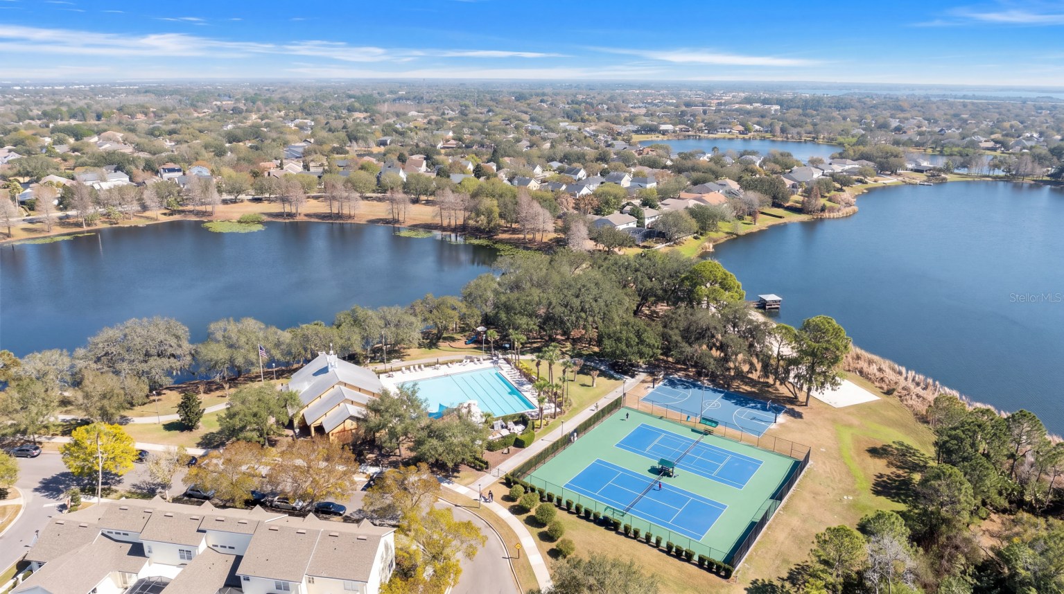 Aerial view of a lakeside community amenity center with a pool, tennis and basketball courts, surrounded by homes and lakes in the Independence and Signature Lakes area of Horizon West, Winter Garden FL