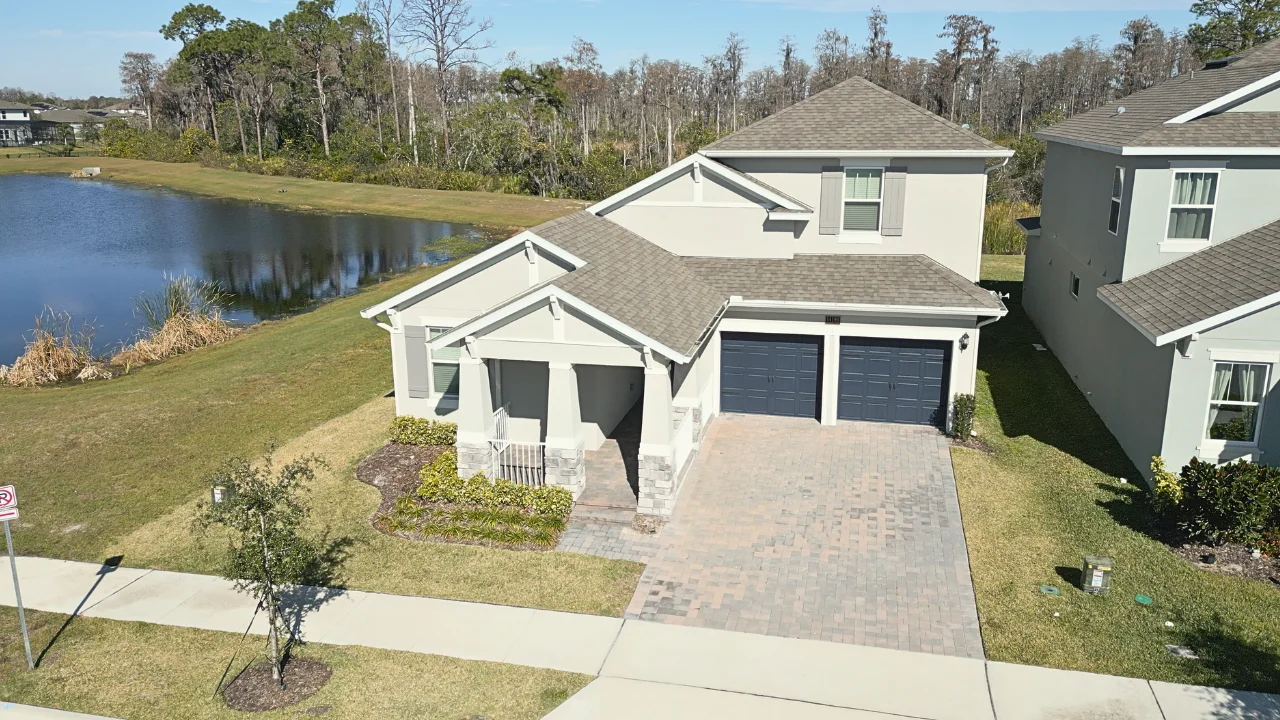 Aerial view of a two-story home with a paver driveway beside a pond at Serenade at Ovation in Horizon West, Winter Garden, Florida