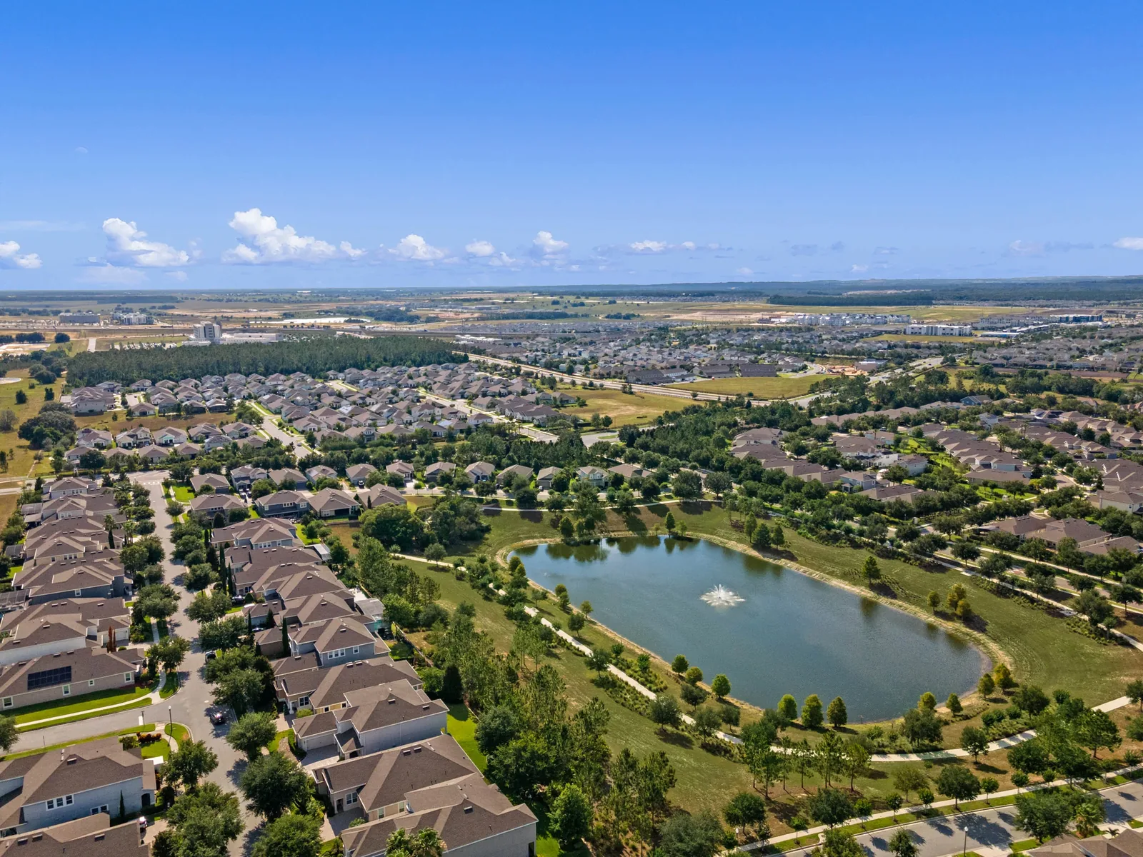 Aerial view of a Taylor Morrison community in Hamlin Town Center, Horizon West, Winter Garden FL, with a fountain pond, walking paths and surrounding neighborhoods.